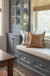 a window seat in the corner of a room next to a wooden table and cabinet