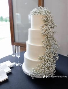 a three tiered wedding cake with baby's breath on the side and wine glasses next to it