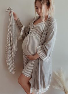 a pregnant woman holding her baby bump while standing next to a white wall with feathers