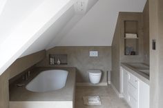 a bathroom with a white bath tub sitting next to a sink and toilet under a slanted roof