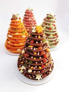 three small christmas trees made out of candies and chocolates on white plates, each decorated in different colors