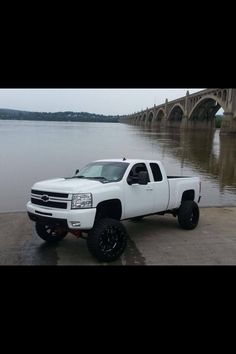 a white truck parked in front of a large body of water next to a bridge