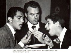 three men in suits and ties are eating food from a plate while another man looks on