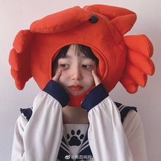 a young boy wearing an orange crab hat and holding his hands up to his face