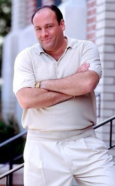 a man with his arms crossed standing in front of some stairs wearing white shorts and a polo shirt