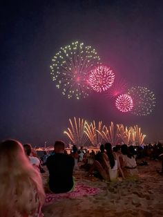 people are sitting on the beach watching fireworks