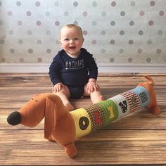 a baby sitting on the floor next to a stuffed dog toy that is made out of crayons