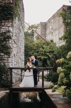 a bride and groom standing on a bridge in front of an old building with water