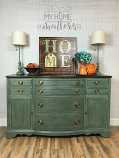 a green dresser with two lamps and a sign above it