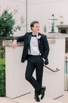 a man in a tuxedo leaning against a wall