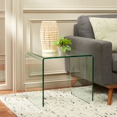 a glass table sitting on top of a wooden floor next to a gray couch and white rug