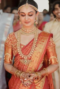 a woman in an orange and gold bridal outfit holding her hands together with other people behind her