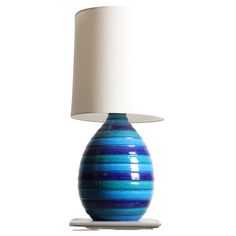 a blue and white striped lamp with a white shade on the top, sitting on a table