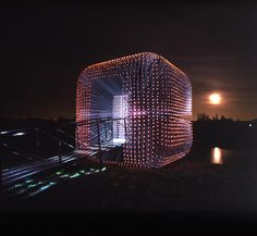 a lit up structure sitting on the side of a body of water with a full moon in the background