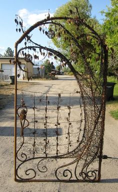 an iron gate with vines on it in the middle of a dirt road next to trees