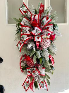 a red and white christmas wreath hanging on the front door with evergreen leaves, candy canes and bows