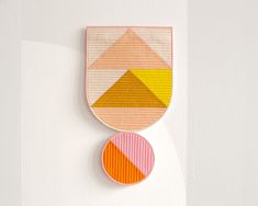 a piece of art hanging on the wall next to a vase with an orange, yellow and pink geometric design