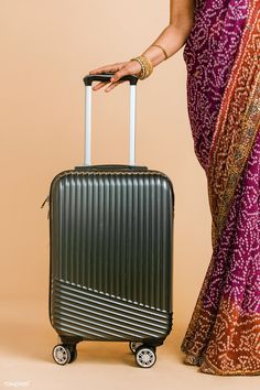 a woman in sari holding onto a black piece of luggage with her hand on the handle