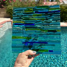 a hand holding up a piece of glass next to a swimming pool with blue water