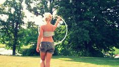 a woman standing in the grass with a hula hoop on her hand and trees in the background