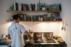 a man standing in front of a stove top oven next to a shelf filled with books