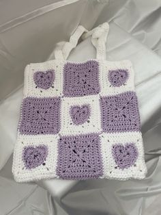 a purple and white crocheted bag sitting on top of a bed