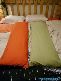 three pillows are laying on top of each other in the same bed, one has an orange and green pillow