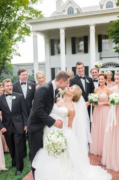 a bride and groom kissing in front of their wedding party