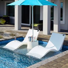 two lounge chairs with an umbrella in the middle of a swimming pool next to a house