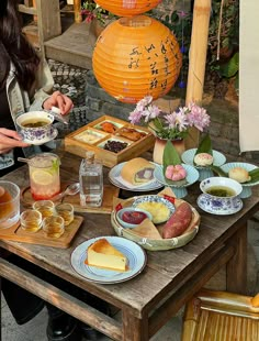 a woman sitting at a table with food and drinks on it, in front of an orange lantern