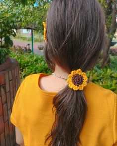 the back of a woman's head wearing a yellow shirt and a flower in her hair