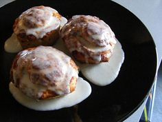 three cinnamon rolls with icing on a black plate