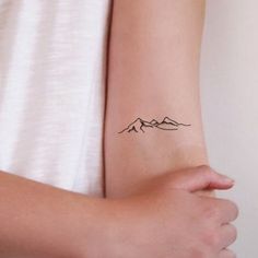 a woman's arm with a tattoo on it that has mountains in the background