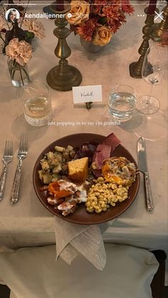 a plate of food on a table with silverware and flowers in vases behind it