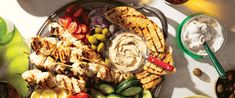 a platter filled with grilled chicken, vegetables and dips on a table