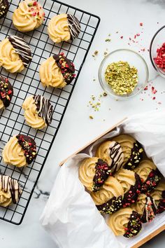 some cookies are sitting on a cooling rack next to bowls of sprinkles and confetti