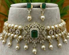 a necklace and earring set with pearls, emeralds and diamonds on a white mannequin