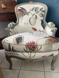 an ornate chair with birds and flowers on the upholstered seat, in front of a blue wall