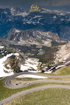 an aerial view of a winding road in the mountains with snow on the top and below