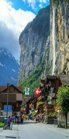 people are walking down the street in front of some buildings and a large waterfall that is high up in the sky