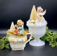 two christmas figurines sitting on top of a teacup next to each other