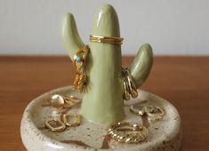 a ceramic cactus with rings on it sitting on a table next to other jewelry items