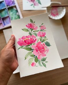 a person holding up a card with watercolor flowers on it