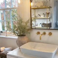 a white sink sitting under a bathroom mirror next to a bathtub and window with plants in it