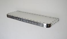 a metal shelf with rivets on it against a white wall