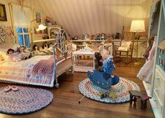 a doll house bedroom with dolls on the bed and in the other room, toys are scattered about