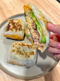 a hand holding a sandwich on top of a white plate next to another piece of food