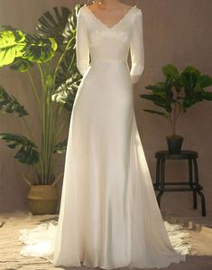 a woman in a white wedding dress standing next to a plant and potted plant