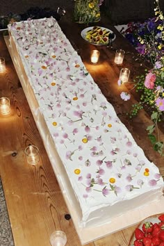 a large cake sitting on top of a wooden table covered in white frosting and flowers