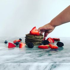 a person is reaching for some fruit on top of the pancakes that they have been placed on